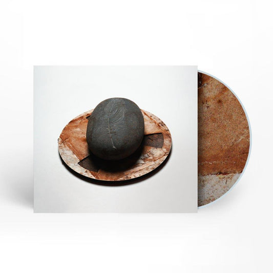 CD cover with a dark stone, feather carving, and wooden texture.
