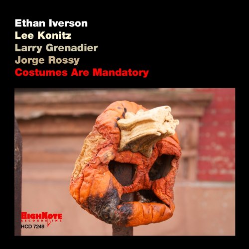 "Album cover with a burnt orange mask on a pole, black background, artist names listed."
