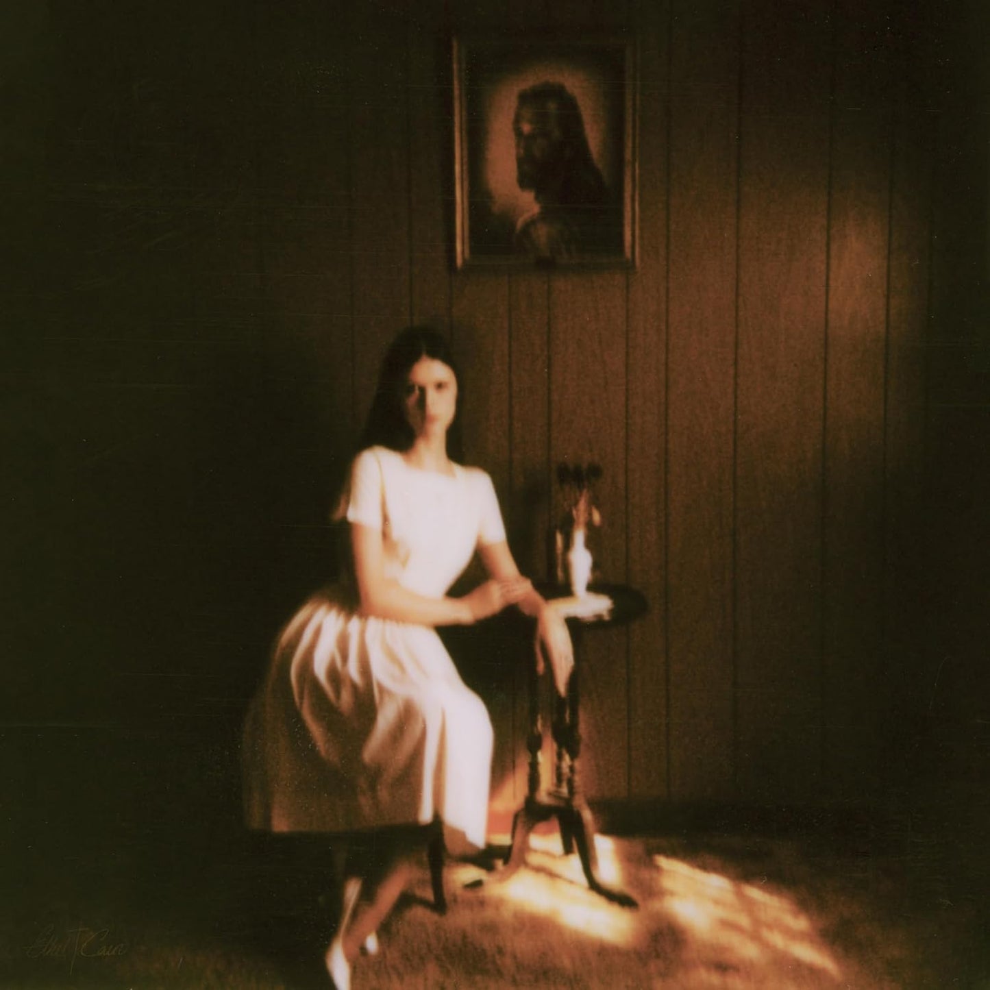 Young woman in a white dress sits in a dimly lit, wood-paneled room.