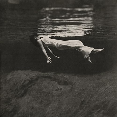 Black and white photo of a person floating underwater in a dress.