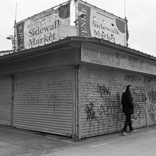 Black and white photo of a person walking past a graffiti-covered storefront.