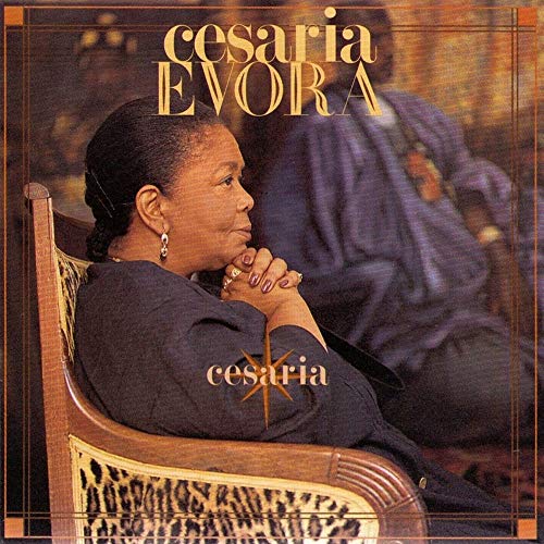 Cesaria Evora sitting in a patterned chair with her hands clasped, album cover art.
