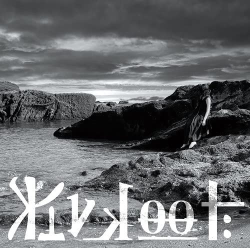 Black and white photo of a person sitting on rocks by the sea.