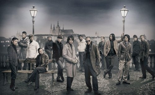 Group of men in coats pose outdoors with a city skyline.