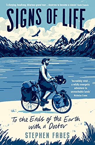 A man on a bicycle with packed gear stands before a lake and mountains.