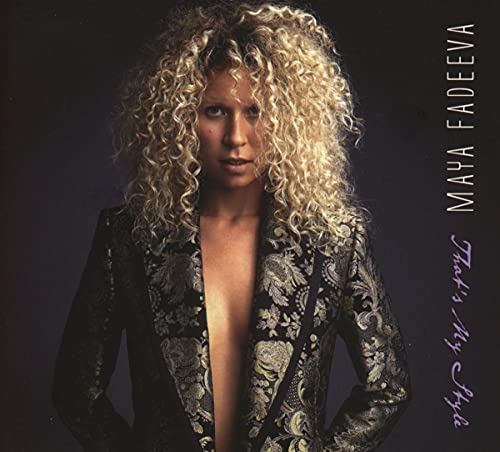 Maya Fadeeva with curly blonde hair wearing a patterned blazer against a dark background.