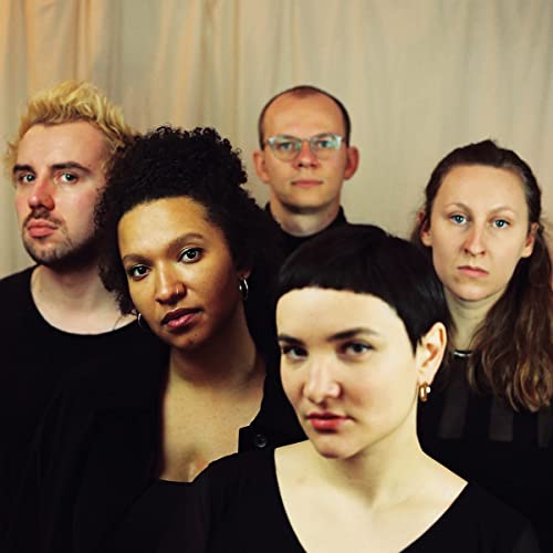 Group portrait of five people wearing black clothing against a plain off-white background.