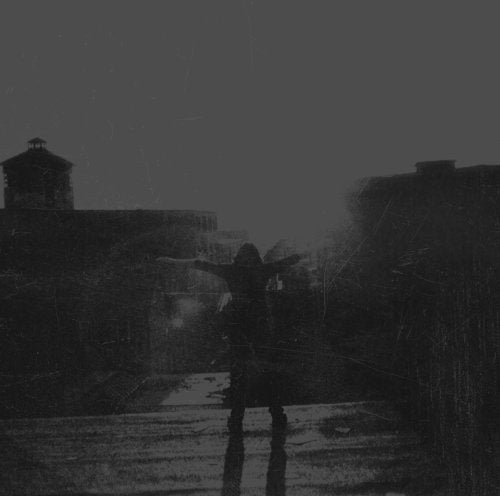 Dark, grainy image of a hooded figure with arms outstretched outdoors.