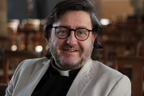 Portrait of a smiling man with glasses and clerical collar in a church.
