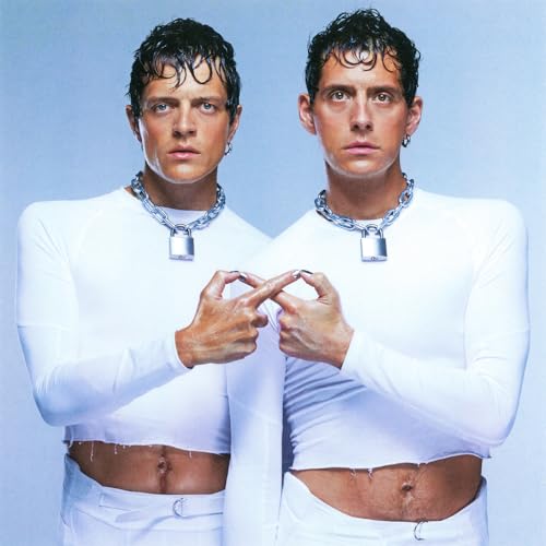 Two identical men in white crop tops and padlock necklaces touch fingers together.