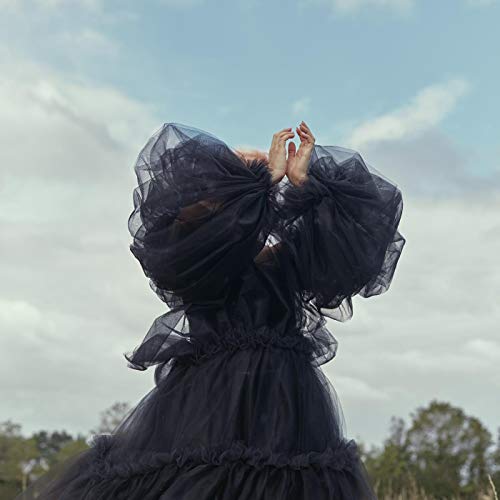 Person in flowing black fabric against a cloudy sky.