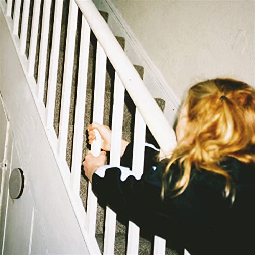 A person with blonde hair holds onto a white staircase railing.