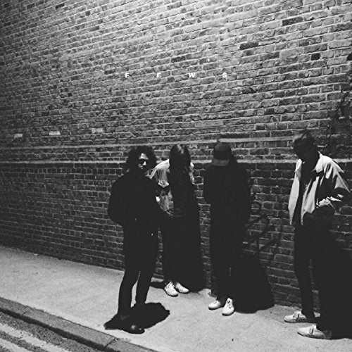 Black and white album cover featuring four figures against a brick wall.