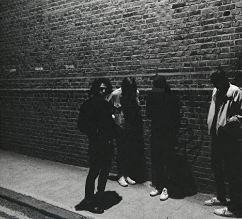 Black and white photo of four figures standing against a brick wall.