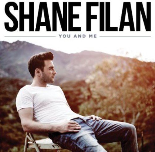 Shane Filan sits on a chair outdoors with mountains in the background.