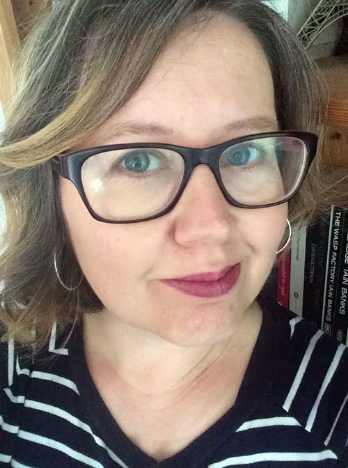 Close-up of a woman with glasses, books blurred in the background.