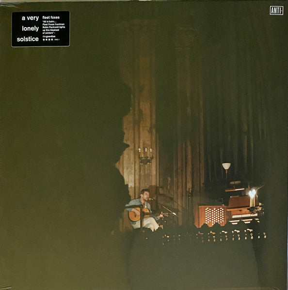 A musician plays acoustic guitar in a dimly lit, cavernous stone building.