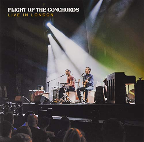 Flight of the Conchords performing live on stage under spotlights in front of audience.
