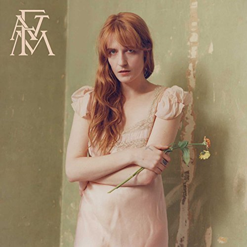 Florence Welch with red hair in a pink dress holding a flower against green wall.