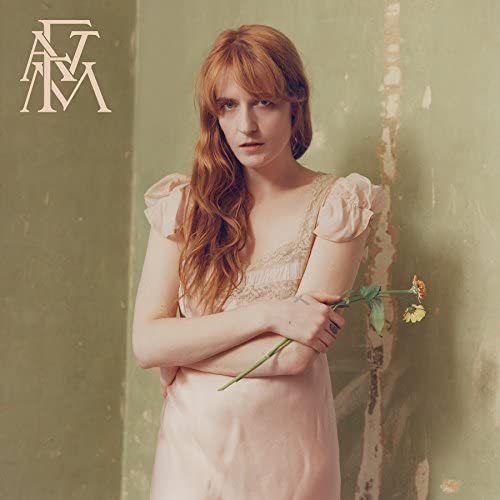 Florence Welch with red hair in a pink dress holding flowers against green wall.