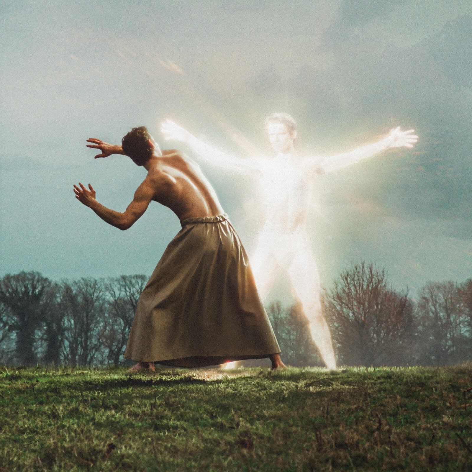 Man in skirt reaching toward a glowing, ethereal figure outdoors.