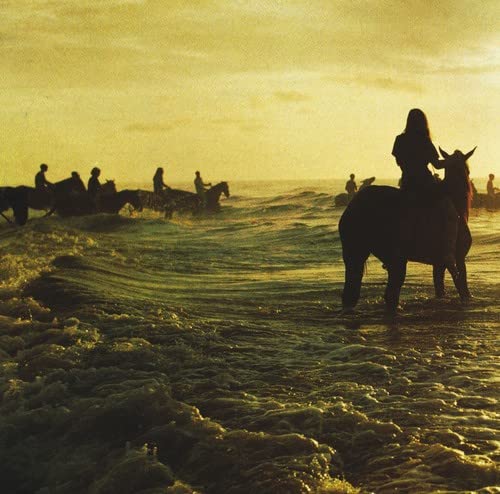 Silhouettes of people on horseback in shallow water at sunset.