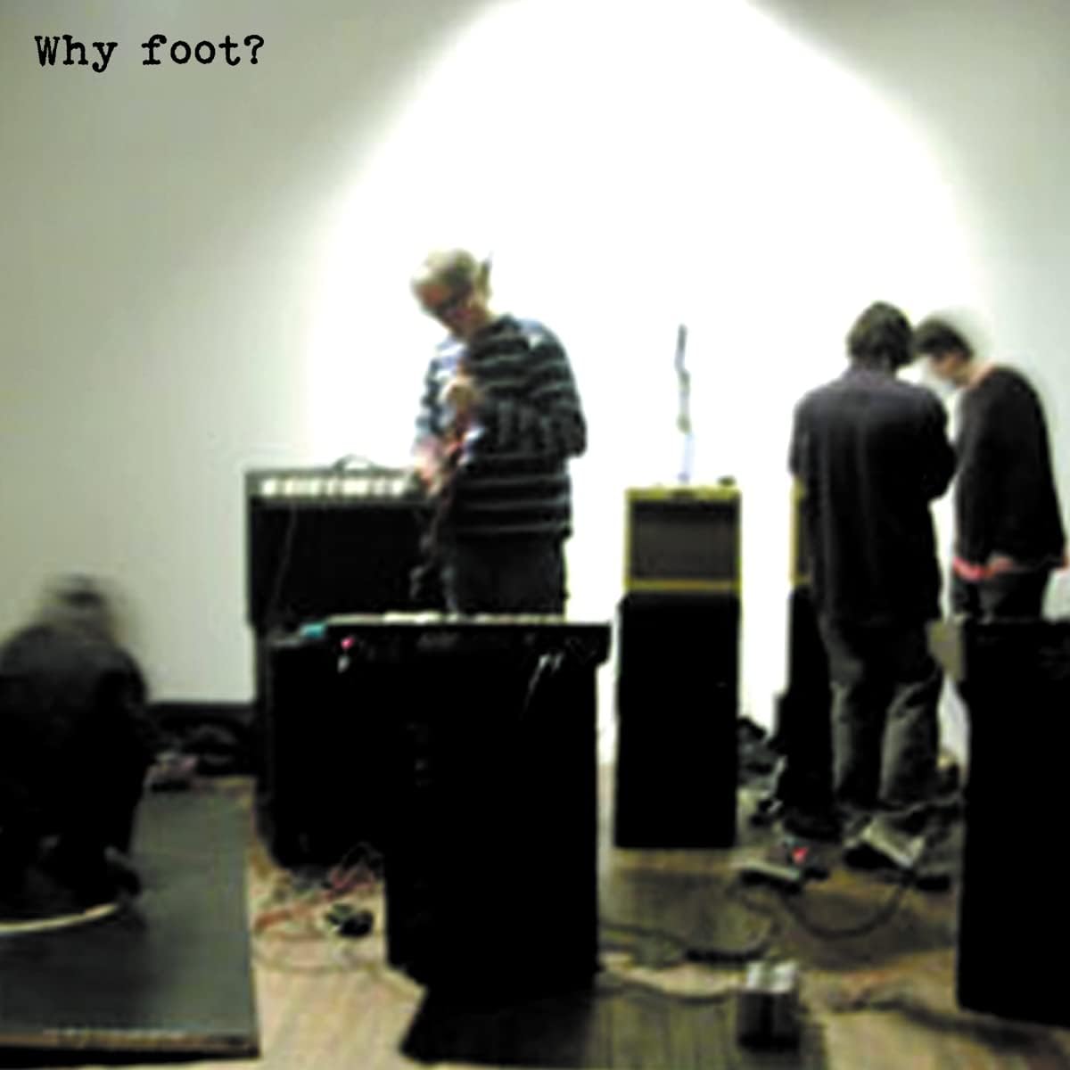 Blurry image of musicians performing with equipment on a wooden floor.