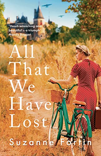 A woman in a red polka-dot dress stands with a bicycle near a castle.