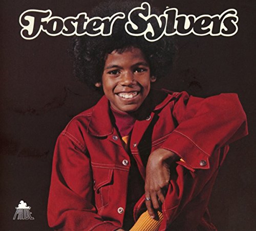 Foster Sylvers smiling, wearing a red jacket, against a dark brown background.