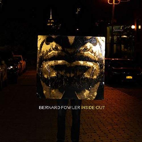 A person holds a square album cover with a distorted face on a dark street.