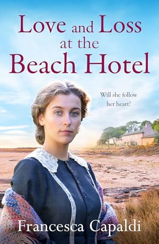 A young woman in vintage clothing stands on a beach before a coastal building.