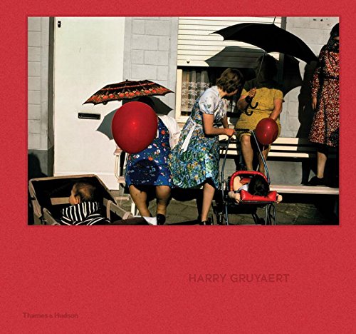 People with umbrellas and red balloons stand near a bench and baby strollers.