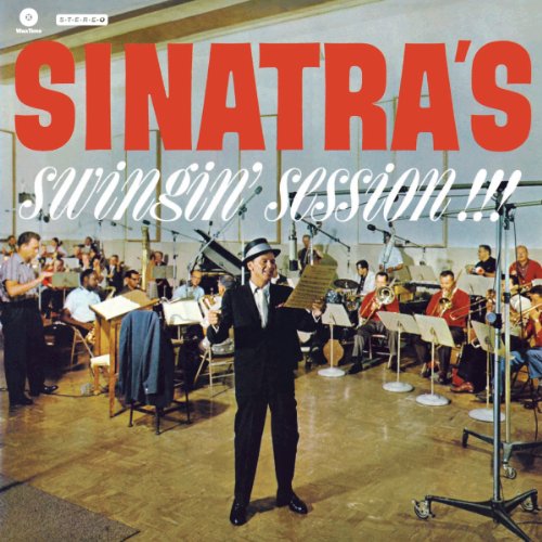 Frank Sinatra in a suit singing in a recording studio with a large orchestra.