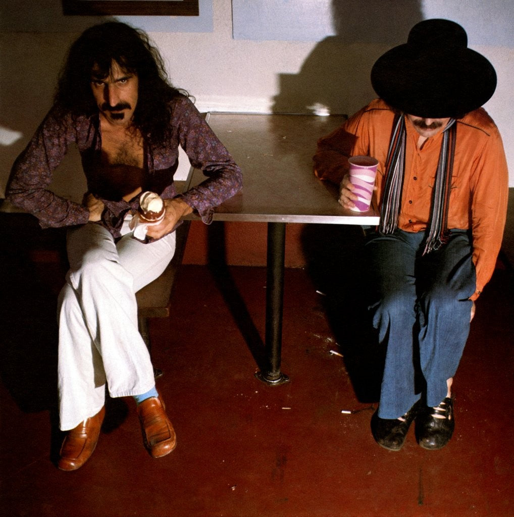 Frank Zappa and Captain Beefheart sitting at a table in a dimly lit room.