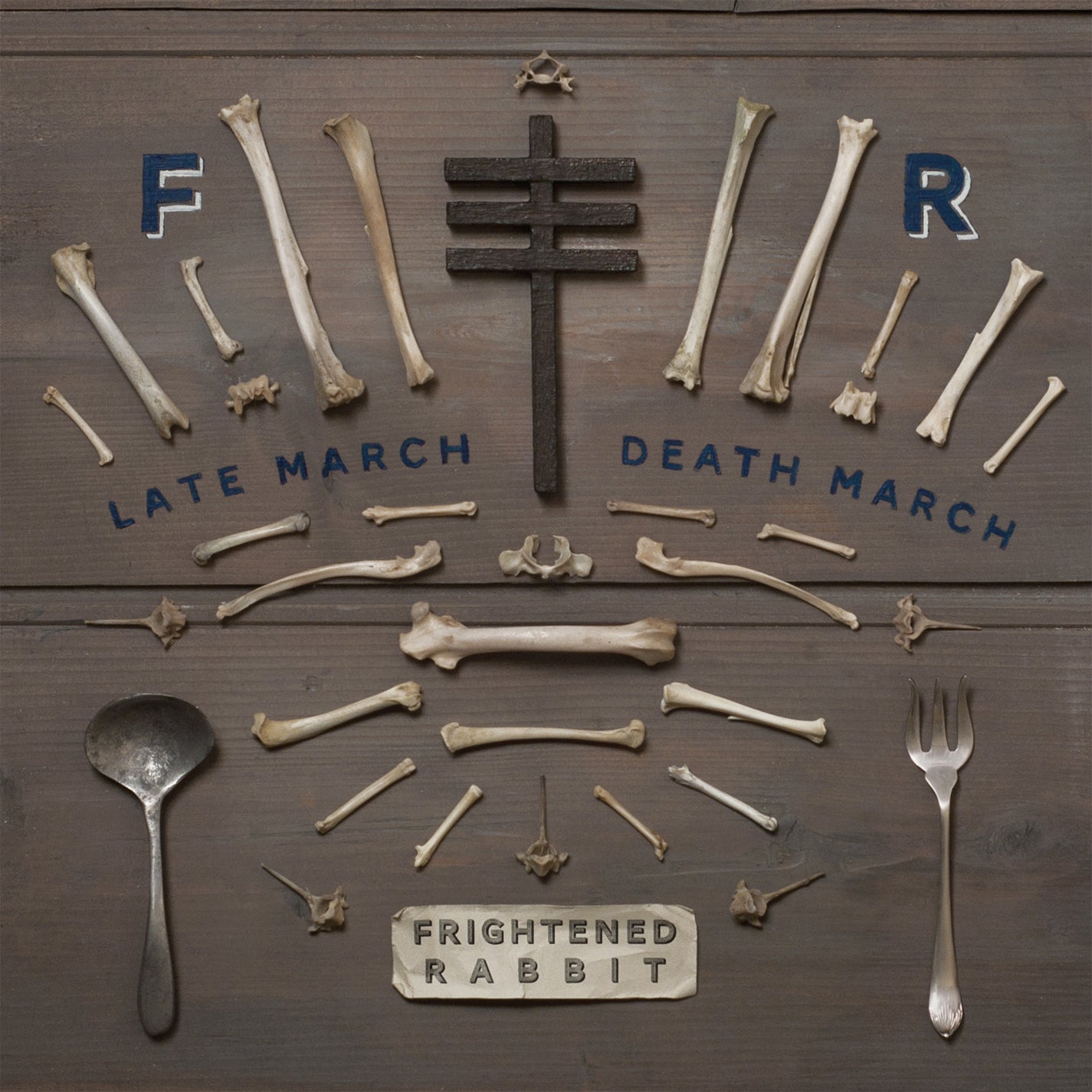 "Album cover with bones, cutlery, and cross on a wooden background."