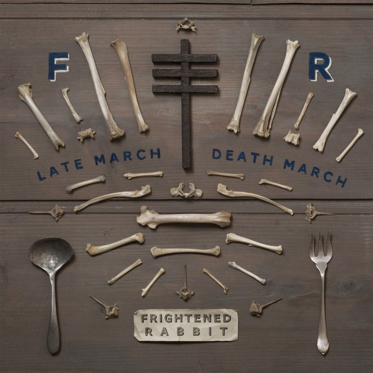"Album cover with bones, cutlery, and cross on a wooden background."