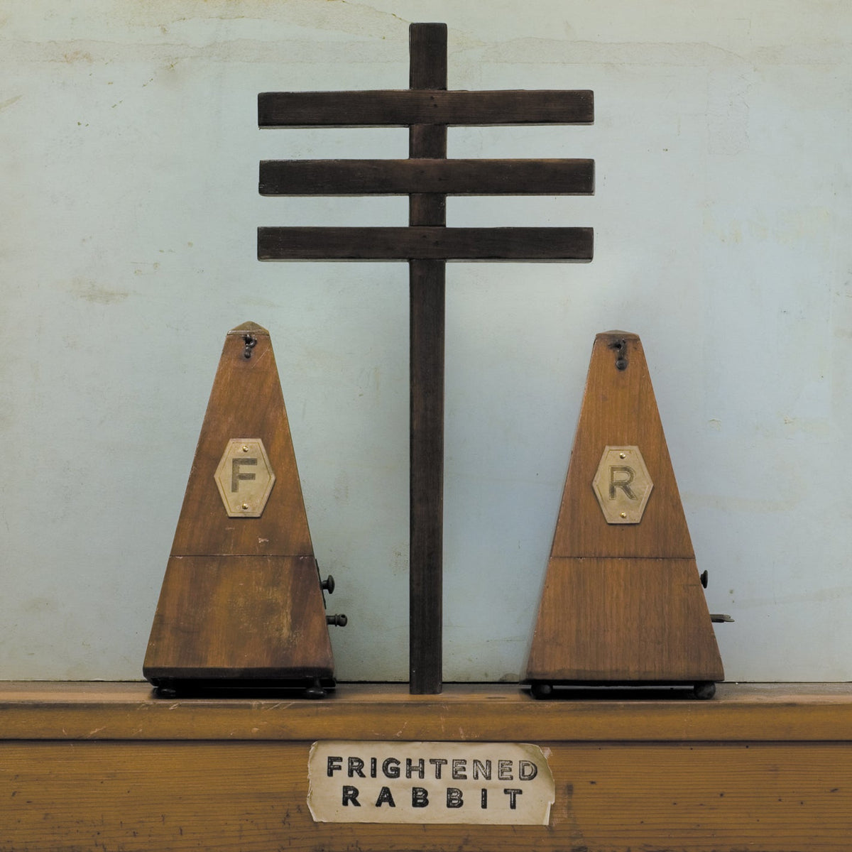 "Two wooden cones labeled 'F' and 'R' with a cross on a shelf."