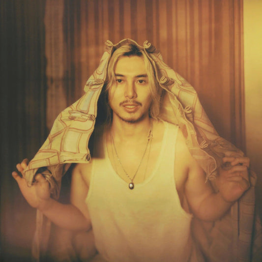 Fujii Kaze wearing a white tank top and holding a patterned fabric over his head.