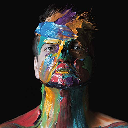 Man's face and upper body covered in thick, multicolored paint against a black background.