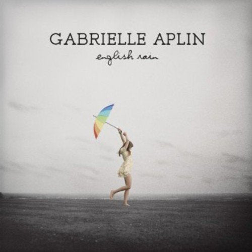 "Album cover: woman in white dress holding rainbow umbrella, running in a grey landscape."