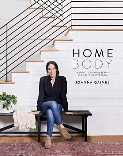 Joanna Gaines sits on a bench in front of a white staircase.