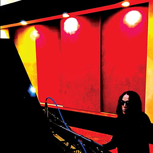 Diamanda Galás wearing sunglasses in a recording studio with bright red and yellow lighting.