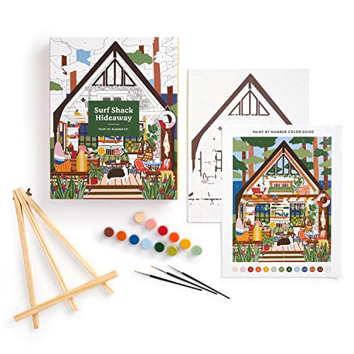 Paint by number kit with a coastal shack illustration, brushes, and paints.