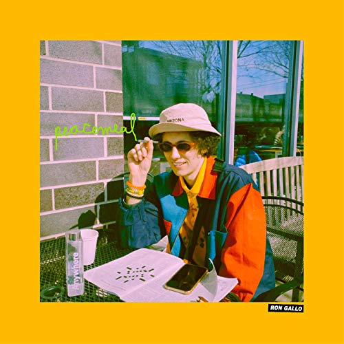 A person wearing a bucket hat and sunglasses sits at a table with a newspaper.