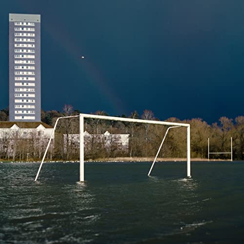 Flooded soccer goalposts in front of a building and trees.