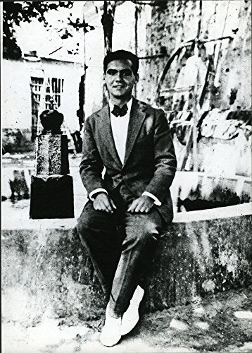 Black and white portrait of a man in a suit, seated outdoors.