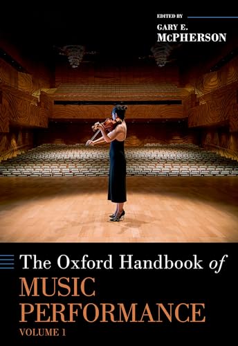 A violinist in a black dress performs on a stage in an empty concert hall.