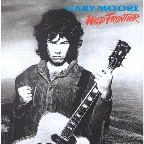 Black and white portrait of Gary Moore holding a guitar against a landscape background.
