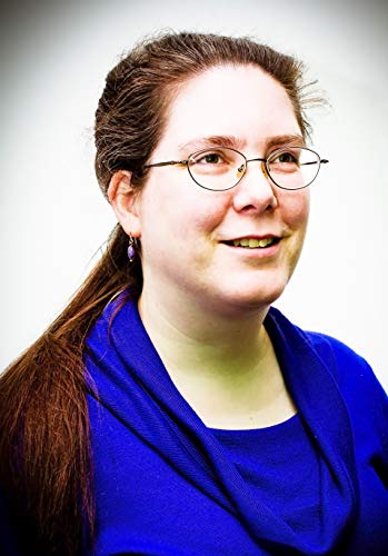 A woman with long brown hair and glasses wearing a blue cowl-neck top.