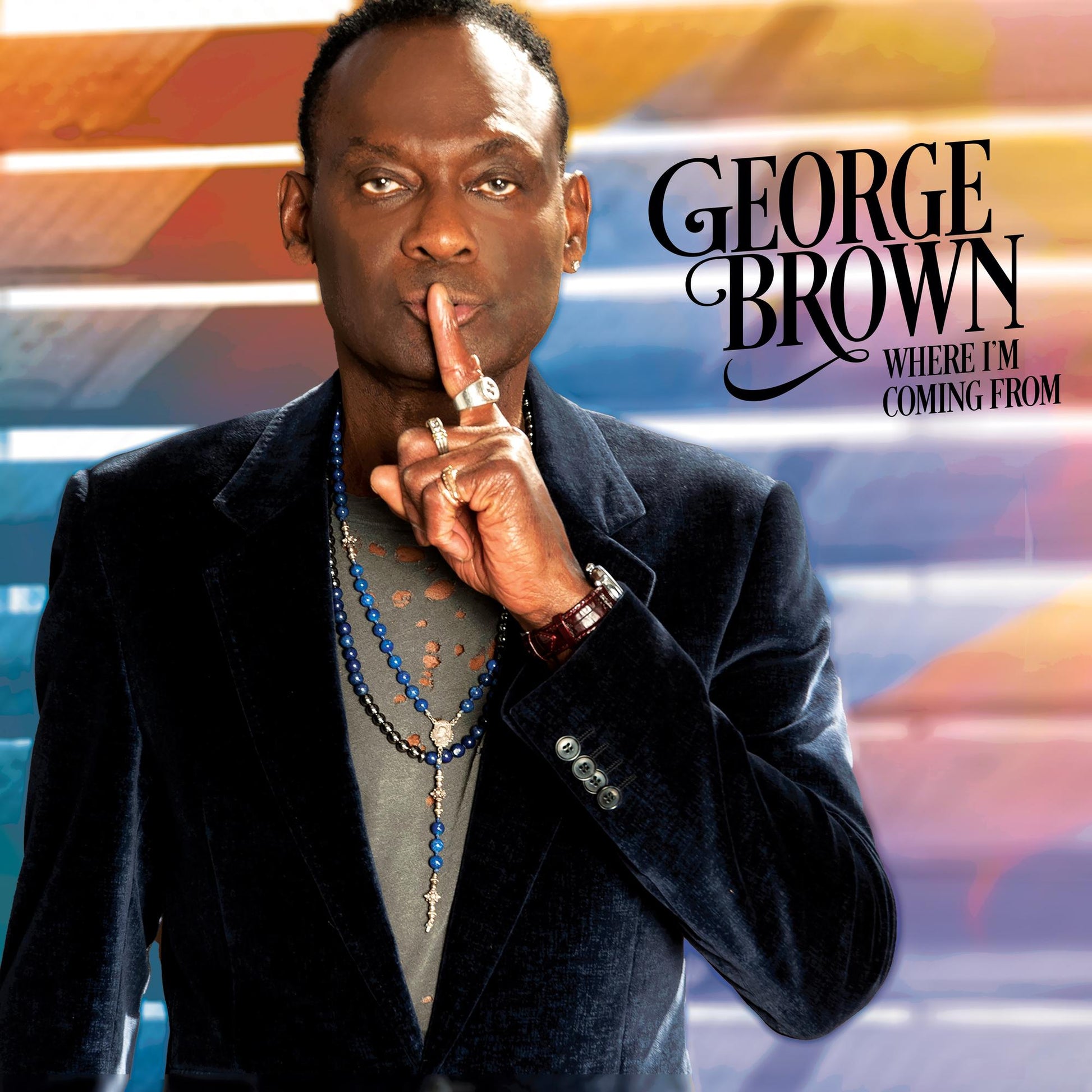 George Brown holding a finger to his lips against a colorful, abstract background.